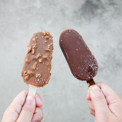 Hands holding vanilla icecreams covered with chocolate and almonds