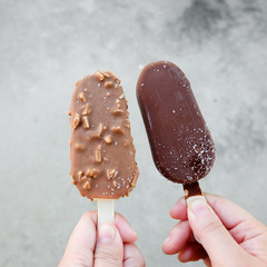 Hands holding vanilla icecreams covered with chocolate and almonds