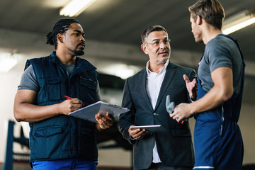 Businessman using touchpad while communicating with auto mechanics in repair shop.
