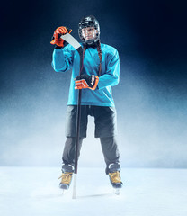 Young female hockey player with the stick on ice court and blue background. Sportswoman wearing...