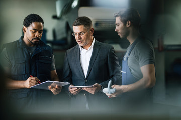 Auto mechanics and their manager analyzing reports in repair shop.