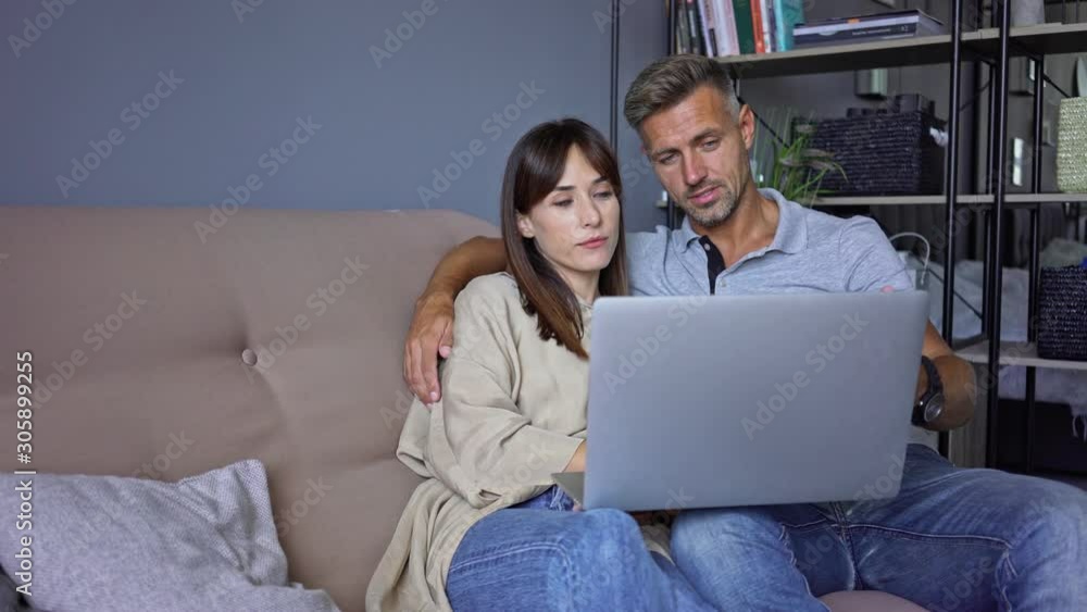 Sticker cheerful couple man and woman smiling and speaking to each other while watching laptop on the sofa a