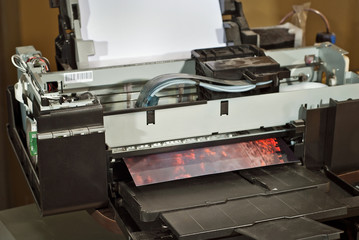 Old broken printer in workshop. The concept of cleaning and calibrating printers. Sunset and red sky with clouds in the photo. Picturesque nature photo printed on printing equipment.