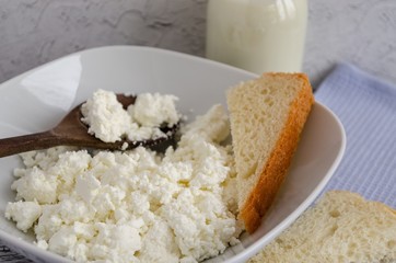 Cottage cheese in a plate, milk in a bottle on a wooden table and a napkin. Healthy breakfast