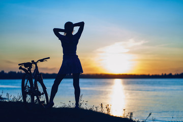 silhouette of a young girl with a bicycle on a background of the sea at sunset
