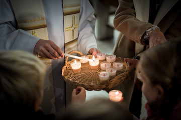 People gathering around Priest lighting candles - obrazy, fototapety, plakaty
