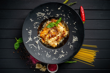 Meat lasagna with beef and tomato sauce on a black plate on a dark wooden background. The concept of Italian cuisine - obrazy, fototapety, plakaty