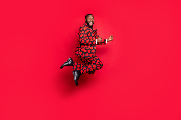 Full body profile photo of funny dark skin guy jumping high traveler abroad shopaholic wear stylish hearts pattern suit blazer shirt tie pants isolated red color background