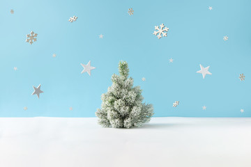 Creative layout with snowy Christmas tree, stars and snowflakes on bright blue background. Minimal winter nature holiday scene.