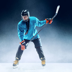 Obraz premium Young female hockey player with the stick on ice court and blue background. Sportswoman wearing equipment and helmet practicing. Concept of sport, healthy lifestyle, motion, movement, action.