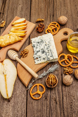 Cheese plate antipasti with smoked and blue cheese, crackers, honey, walnuts and ripe pear. Traditional snack recipe idea. Wooden boards background