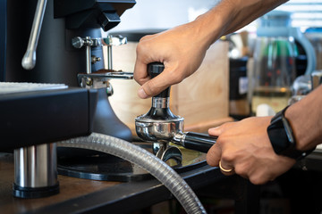 Coffee barista is pressing coffee beam into the filter block by using a temper. Close up and selective focus. Fresh coffee making photo action.