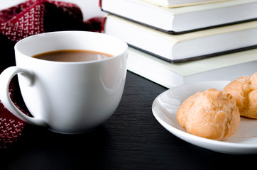 A round white cup and saucer stands on a white wooden table next to books and yellow autumn leaves