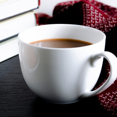 A round white cup and saucer stands on a white wooden table next to books and yellow autumn leaves