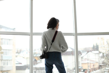 portrait of a beautiful hipster girl with a camera standing by the window