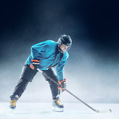 Obraz premium Young female hockey player with the stick on ice court and blue background. Sportswoman wearing equipment and helmet practicing. Concept of sport, healthy lifestyle, motion, movement, action.