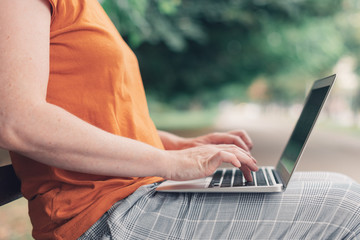 Naklejka premium Woman using laptop computer on park bench