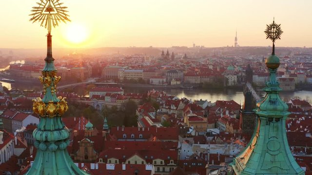 Aerial view St. Nicholas church and mala strana district in Prague at sunrise. Drone flying at low above roof of famous cathedral, circling near spires, sun shining through masonic symbol on top. 
