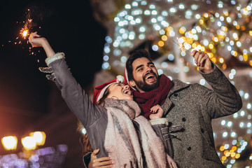 Young loving couple burning sparklers by holiday illumination on new years eve.