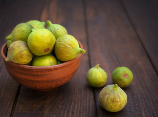 ripe yellow-green figs in a clay plate and three figs lying on a wooden table