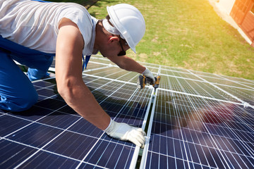 Professional worker installing solar panels on the green metal construction, using different...