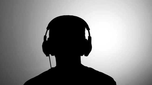 Mens black silhouette against grey wall listen to music wearing headphones