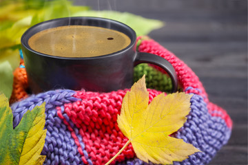 Black coffee in a black mug wrapped in a warm, colored, knitted scarf, and autumn leaves