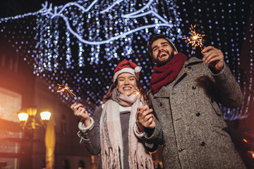 Young loving couple burning sparklers by holiday illumination on new years eve.