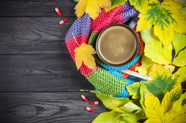 Autumn still life: A cup of hot coffee and a thermometer wrapped in a warm scarf, yellow leaves....
