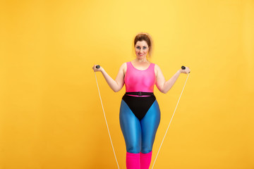 Young caucasian plus size female model's training on yellow background. Copyspace. Concept of sport, healthy lifestyle, body positive, fashion, style. Stylish woman practicing with jump rope and