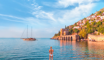 Beautiful young woman in white bikini stands on the sea - Landscape of ancient shipyard near of...