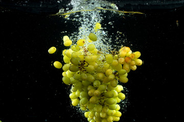 green grape splashing into water in black background