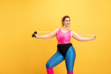 Fototapeta na wymiar Young caucasian plus size female model's training on yellow background. Copyspace. Concept of sport, healthy lifestyle, body positive, fashion, style. Stylish woman practicing with jump rope and