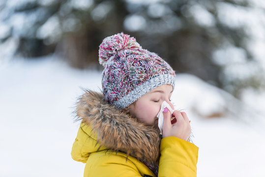 Young girl with handkerchief outdoor in snow cold park. Woman blows her nose in winter