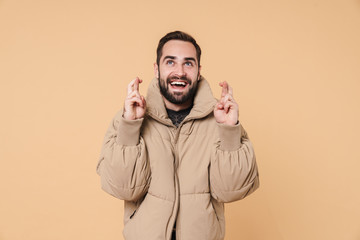 Image of young man in winter jacket smiling and keeping fingers crossed