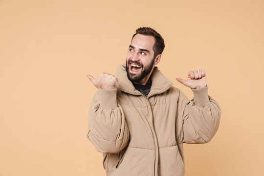 Image of positive man in winter jacket smiling and pointing fingers aside