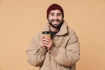 Image of young man in winter jacket and hat smiling while drinking coffee