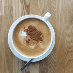 White cup with coffee and cinnamon on a wooden table.