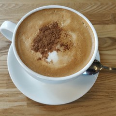 White cup with coffee and cinnamon on a wooden table.