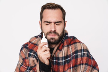 Portrait of ill guy wrapped in blanket holding nose drops due to flu