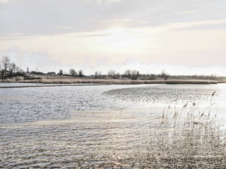 The mixed image of the view of the ice on the surface of the lake and the natural background of the view of the lake shore at the cold spring day at the City Park. 