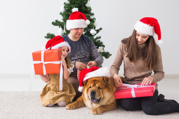 Pet, holidays and festive concept - Family with dog are sitting on floor near christmas tree.