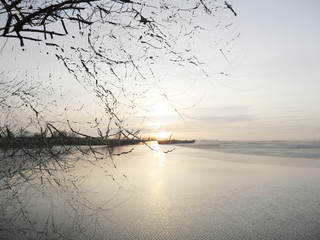 The mixed image of the view of the ice on the surface of the lake and the natural background of the view of the lake shore at the cold spring day at the City Park. 