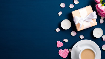 Valentines Day background with coffee cup, roses flowers bouquet, petals, gift box, candles on dark blue. Flat lay style composition, top view. Love and romance concept.