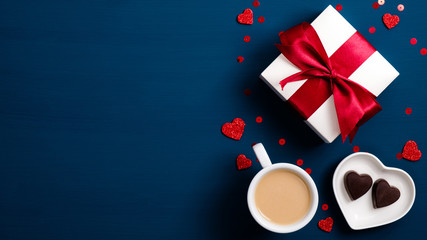 Valentine day concept. Top view gift box, coffee cup, heart shaped candy on blue table. Flat lay...