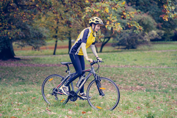 A girl with a bicycle stands on a green lawn in the park