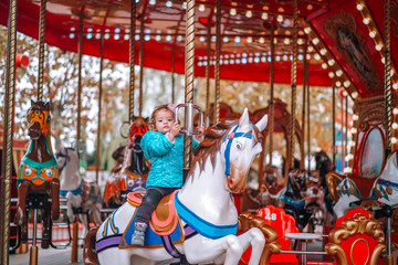 Little girl in a children's amusement park on a carousel. Family leisure at the weekend.