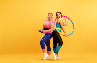 Fototapeta na wymiar Young caucasian plus size female models training on yellow background. Copyspace. Concept of sport, healthy lifestyle, body positive, fashion. Friendship, girl power. Stylish woman practicing, smiling