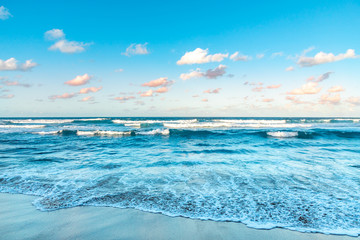 Fototapeta premium Waves on the beach at sunset, pink and turquoise cloudy sky