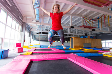Fitness, fun, leisure and sport activity concept - Young happy woman jumping on a trampoline indoors